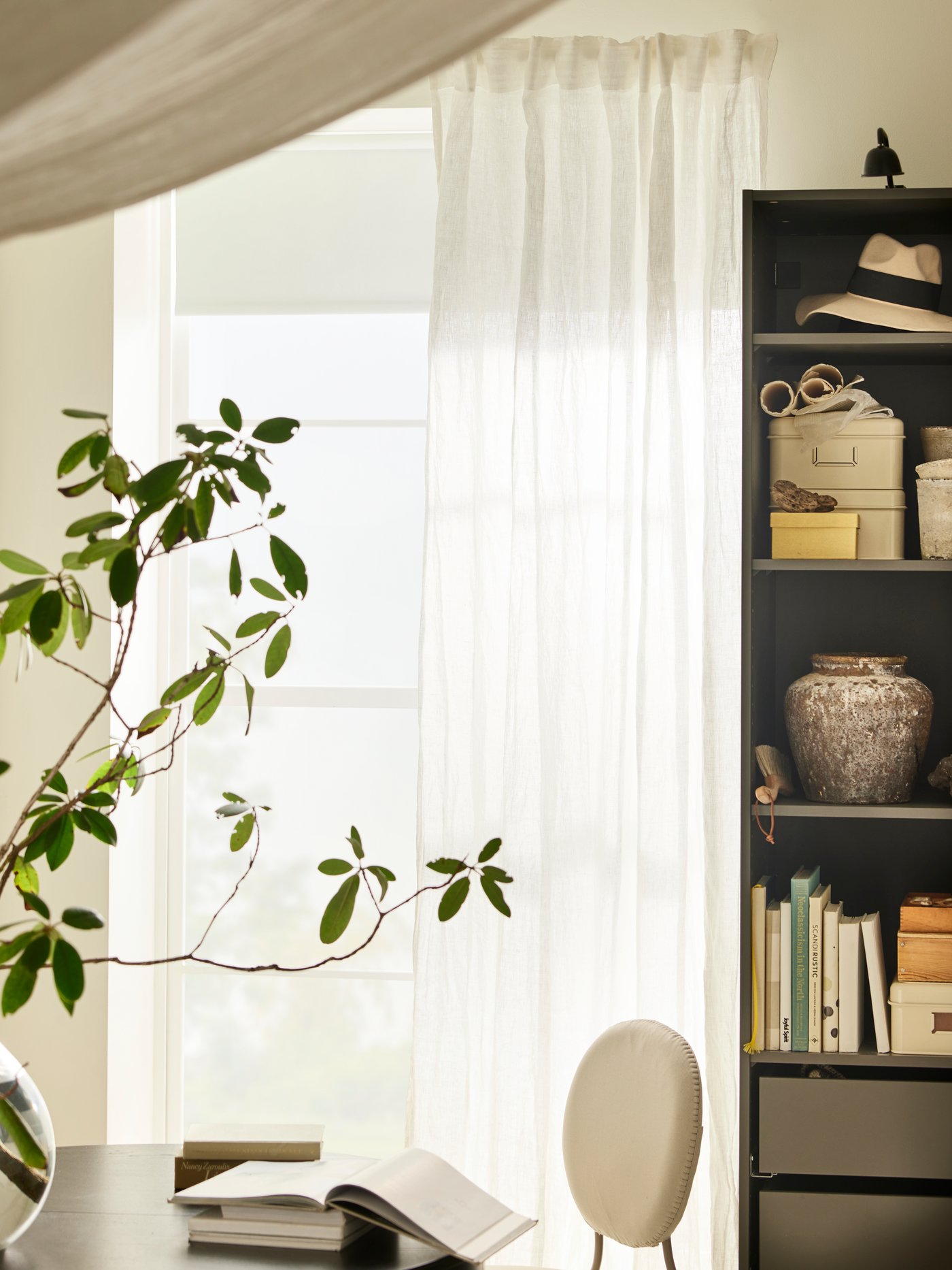 A pair of white DYTÅG curtains hang at a large window along with a white FÖNSTERBLAD block-out blind, with a table in front.