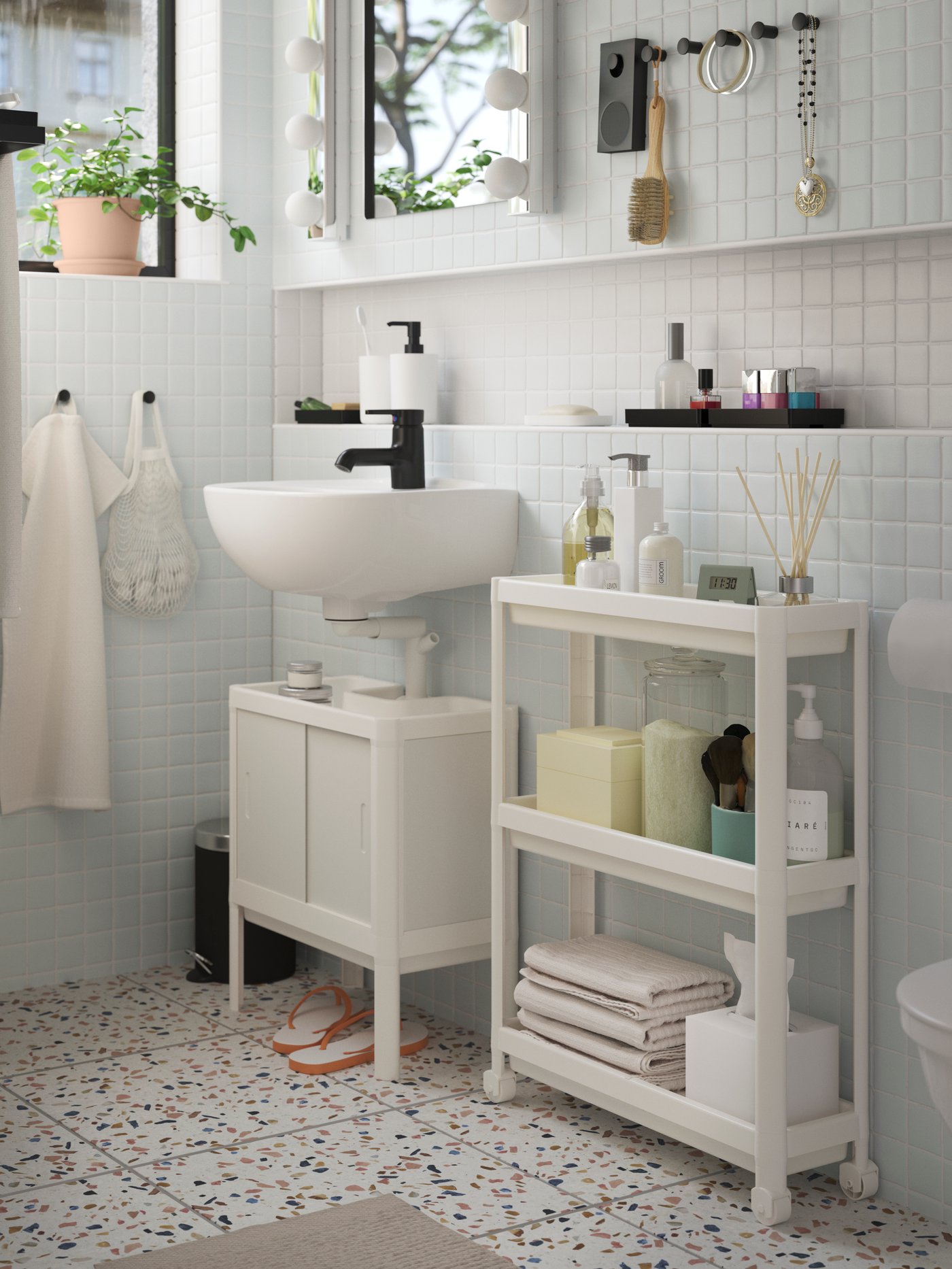 Modernes Badezimmer mit weißen Möbeln, Waschbeckenunterschrank, Regal für Handtücher und Pflegeprodukte, hellblauen Fliesen und Terrazzo-Boden.