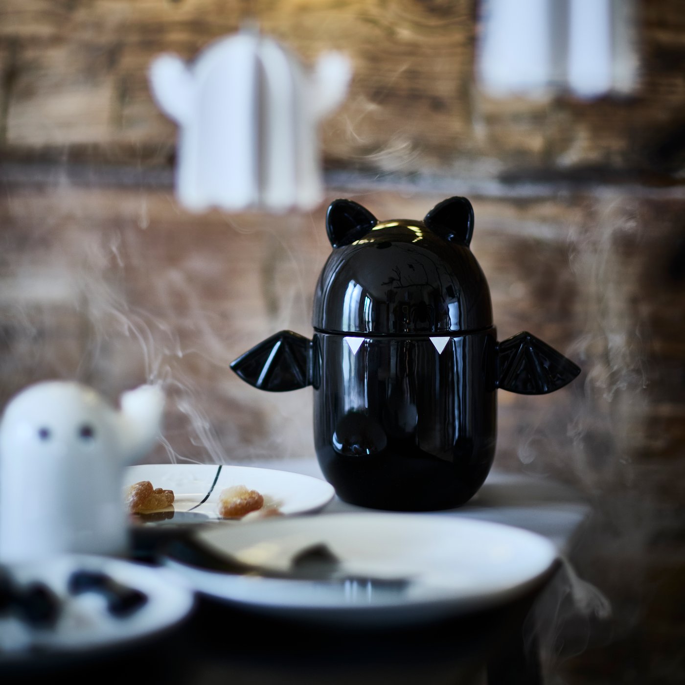 Cuenco KUSTFYR negro con tapa en forma de murciélago, colocado en el comedor como un detalle decorativo inspirado en Halloween.