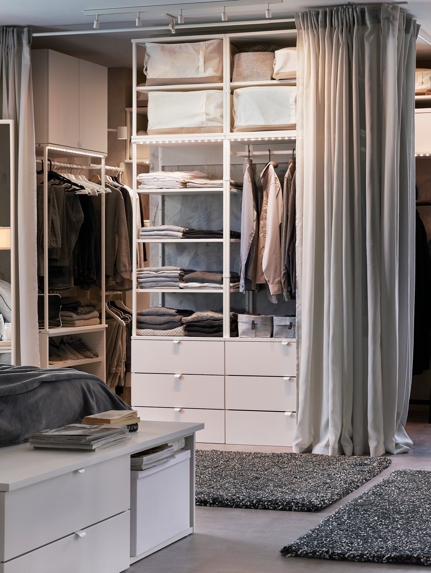 En öppen garderob i ett sovrum med gråa gardiner framför.