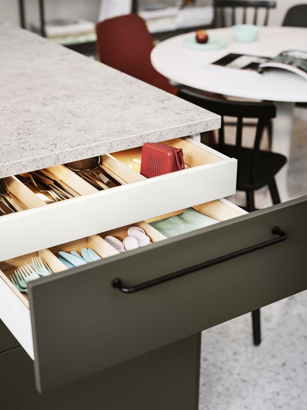An open kitchen drawer with brown-beige HAVSTORP kitchen front showing an inner drawer and cutlery in cutlery trays inside. 