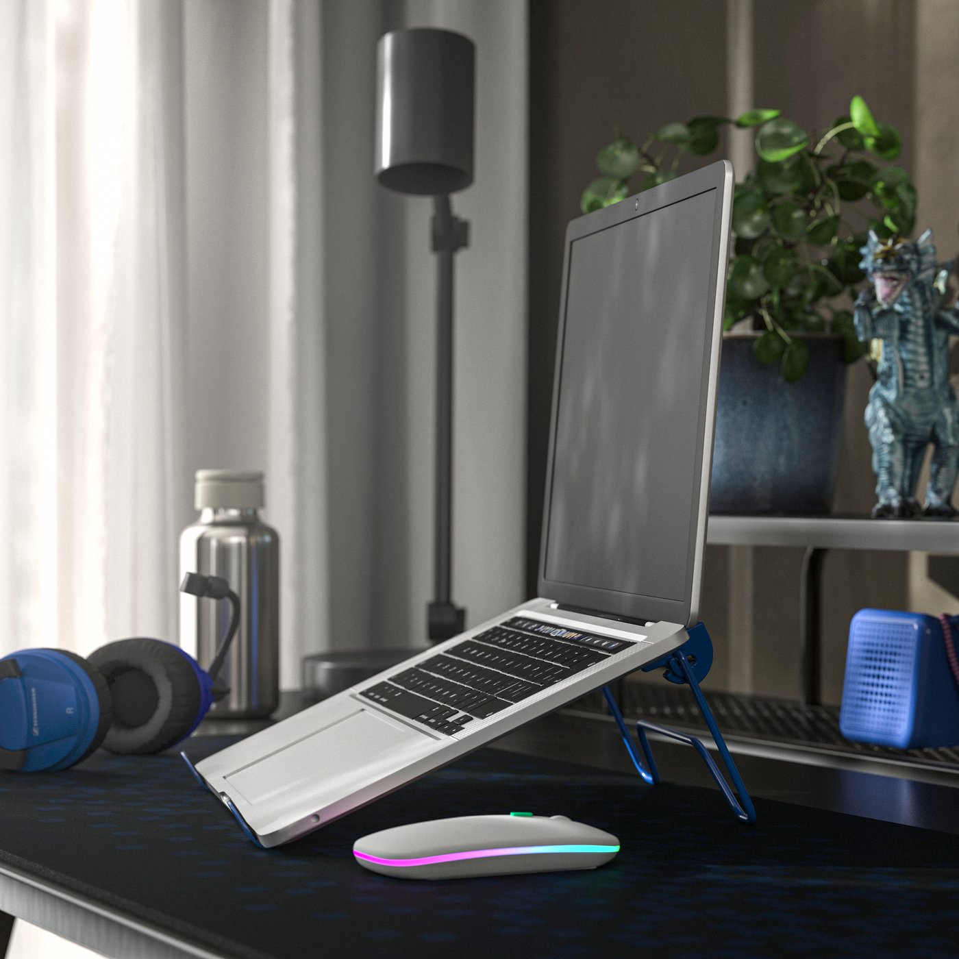 Una scrivania con un PC aperto posto su un supporto LÅNESPELARE. Accanto, delle cuffie, una borraccia aperta e un mouse su un tappetino.