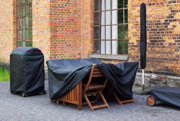 Zu sehen sind die TOSTERÖ Schutzhüllen über einer Outdoormöbelgruppe, einem Grill und einem Sonnenschirm.
