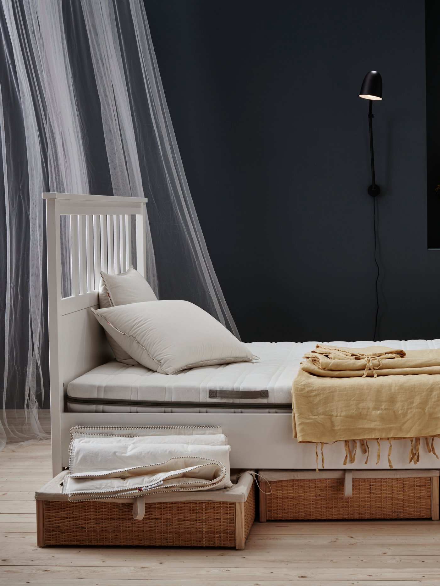 Dormitorio con pared negra, estructura de cama de madera blanca, colchón de espuma, almohadas firmes, lámpara de pared, cajas de almacenaje para cama, cortinas de red.