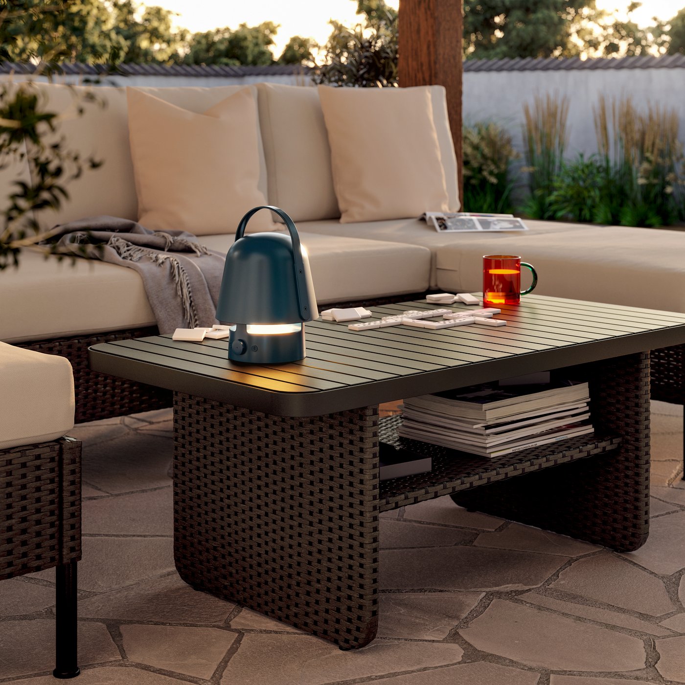 En beige VITTSKÄR modulopbygget loungesofa med puder og en grå HOLMVI plaid samt et mørkegråt sofabord i eftermiddagssolen.