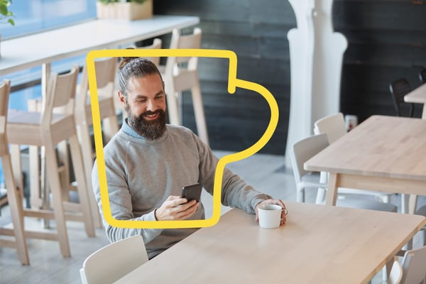 A man looking at his phone smiling while holding a coffee cup in the Swedish Restaurant.