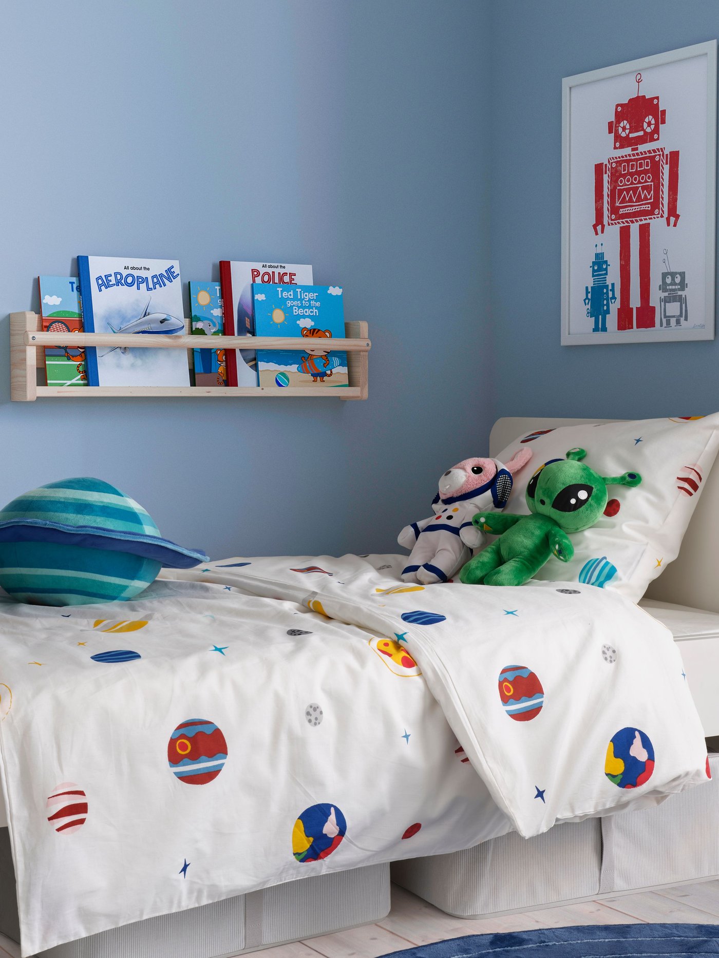 Un dormitorio infantil donde el plumón tiene diseños espaciales y unos peluches de extraterrestres encima. 