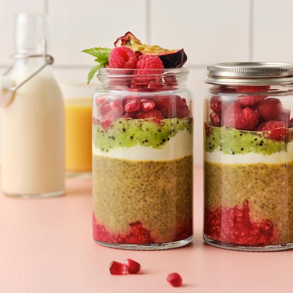 Chia pudding, red berries, kiwi and yoghurt are layered in glass jars with a slice of passion fruit and mint leaves on top. 