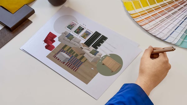 Projektantka wnętrz IKEA prezentująca kartki z wydrukiem kolażu produktowego zaprojektowanego pomieszczenia. Obok na blacie leży wzornik kolorów i próbki materiałów.