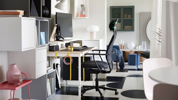 A PC gaming setup with an ash effect/white UTVISNING gaming desk with shelf and a dark grey chair in a white passageway.