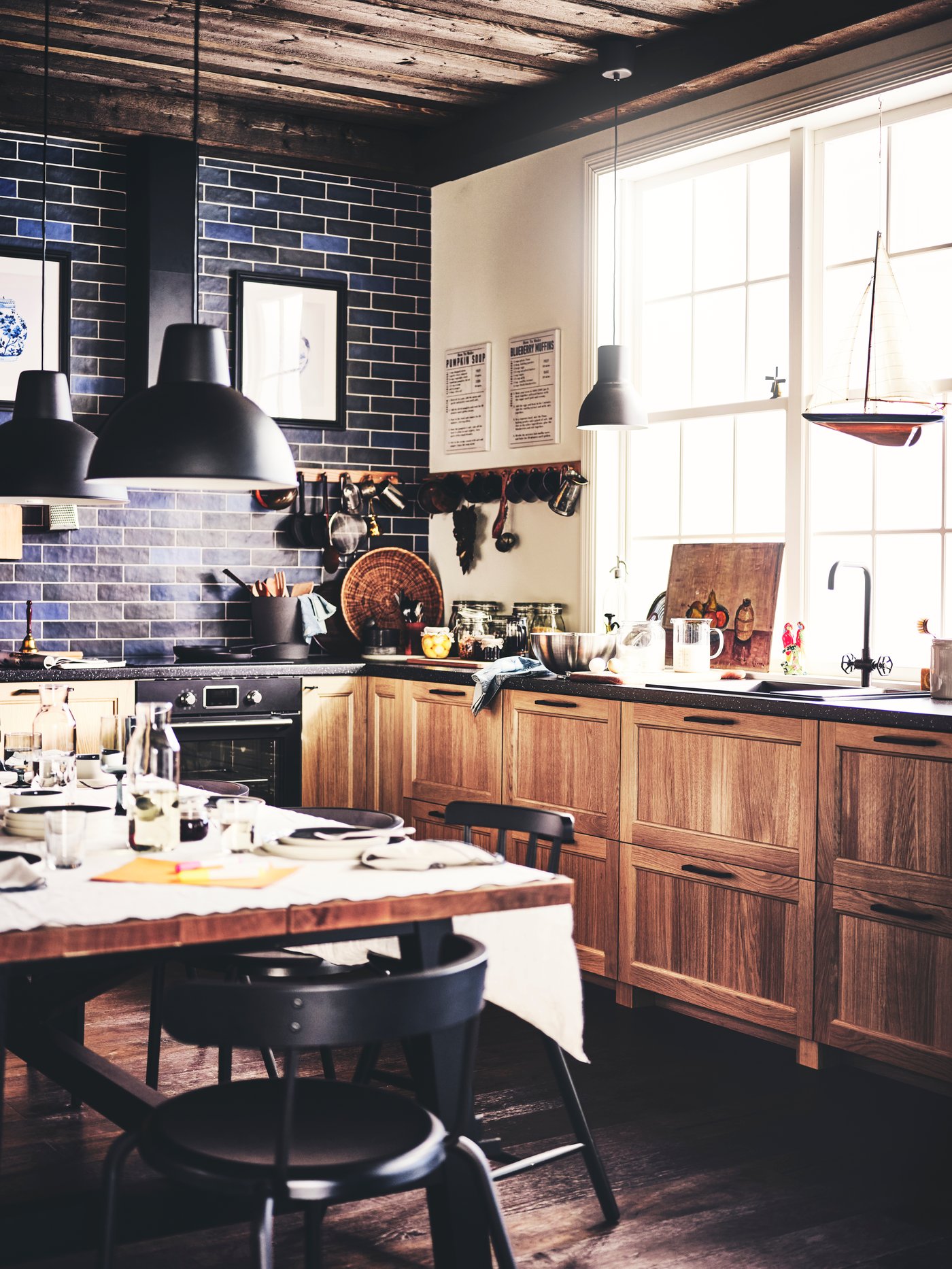 A kitchen with an industrial look, featuring wooden cabinet fronts, a dark worktop, and two black lamps above the dining table.