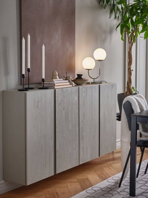Two wall-mounted, pine IVAR cabinets have been painted grey and have candles, books, decorations and a table lamp on top.