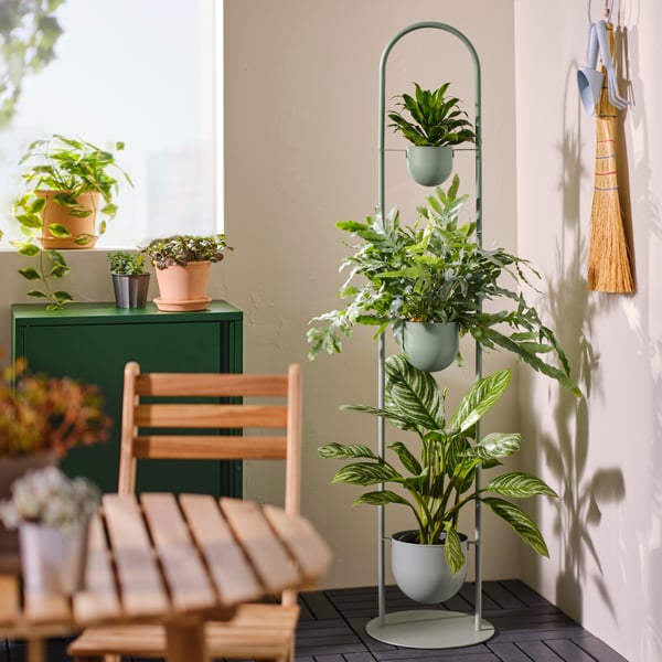 Three potted plants can be seen on a DAKSJUS plant stand. To the left lies an outdoor wooden table and chair set.