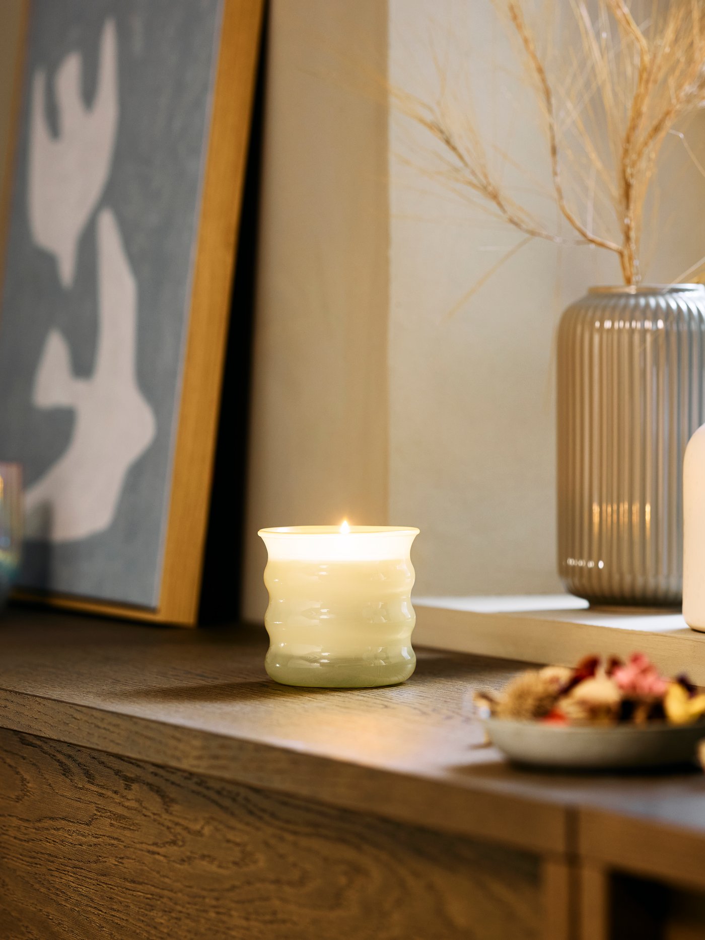 A light yellow JUVELTRAST scented candle on a wooden sideboard in the living room.