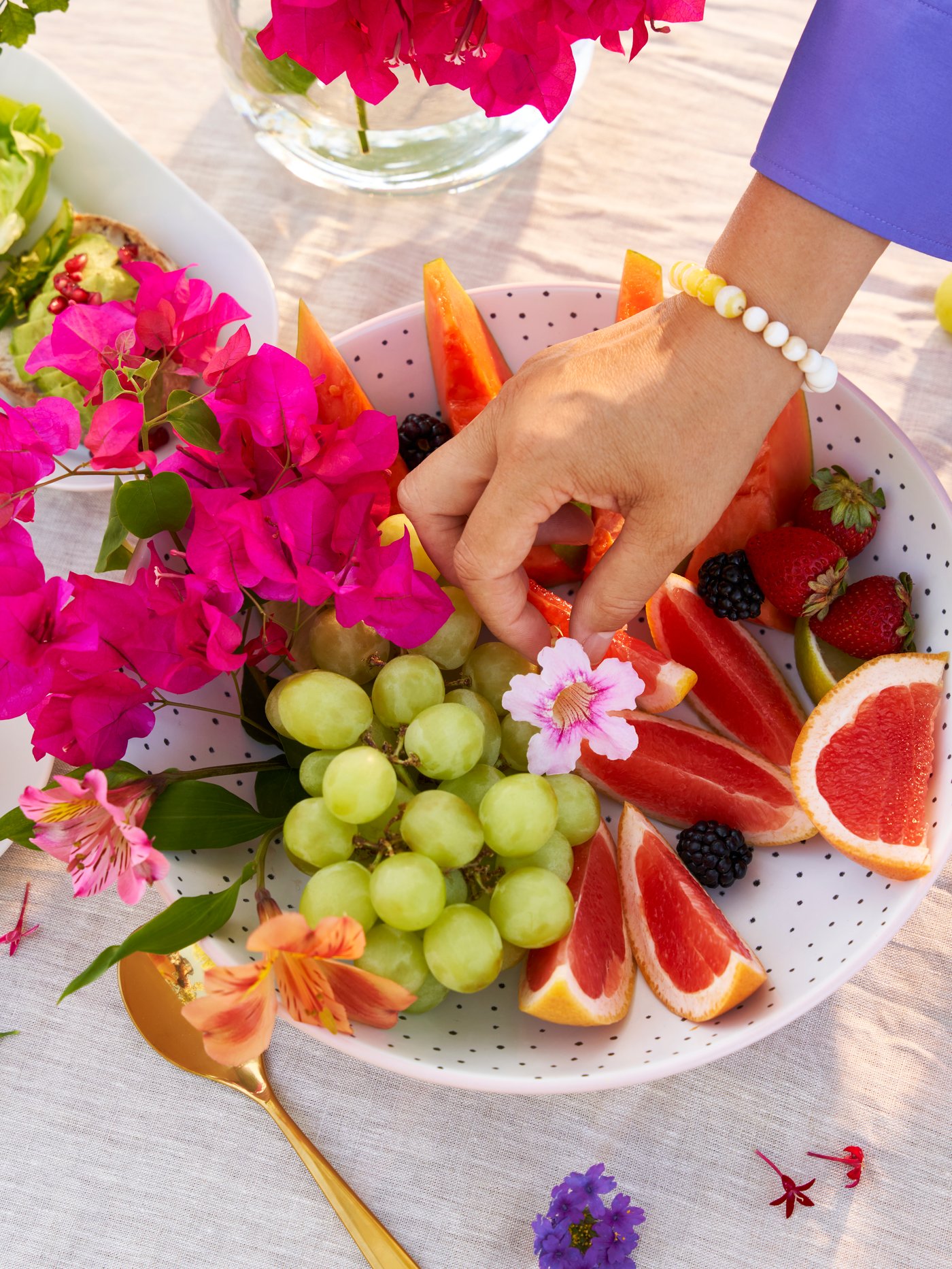 Cocina en la que aparece la mano de una persona colocando una flor sobre varias frutas colocadas en una fuente de servir STENTICKA blanca y rosa.