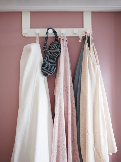 ホワイトのバスローブ、服、マスクが付いたピンクのドアに、ホワイトのスチール製のドアハンガーが付いたプラスチック製のノブが付いている。