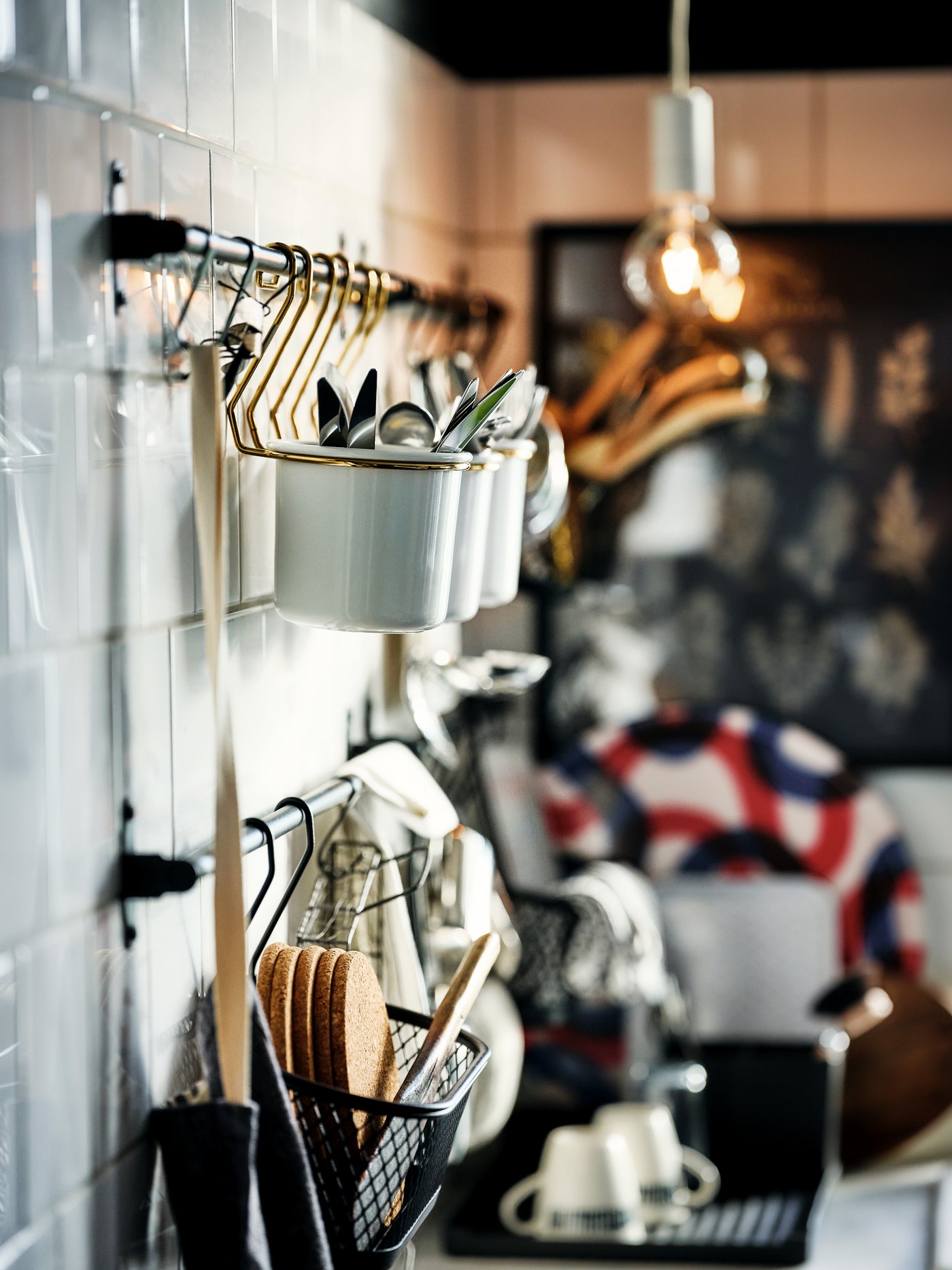 Multiple kitchen accessories held by hooks and containers on black HULTARP rails, fitted on a white-tiled wall.