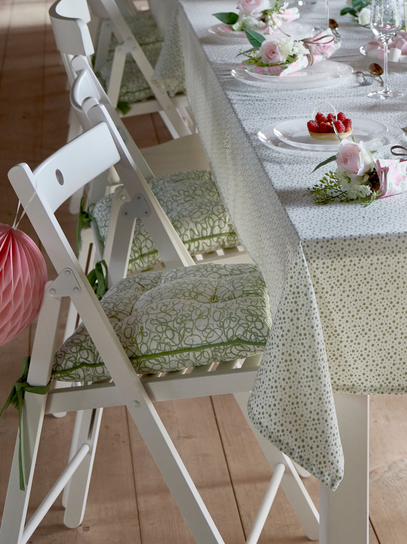 Tavola apparecchiata con tovaglia bianca e verde INBJUDEN e con sedie bianche pieghevoli TERJE con cuscini verde e bianco INBJUDEN 