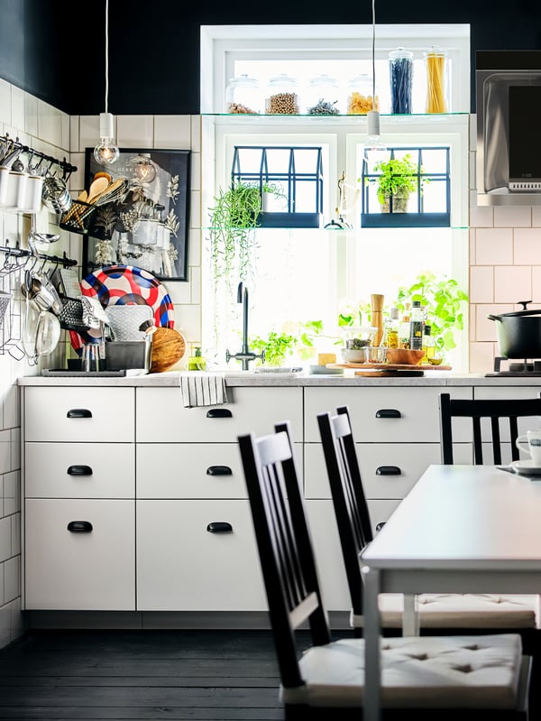 A corner of a black-and-white kitchen with white base cabinets and multiple utensils on rails fitted on a white-tiled wall.