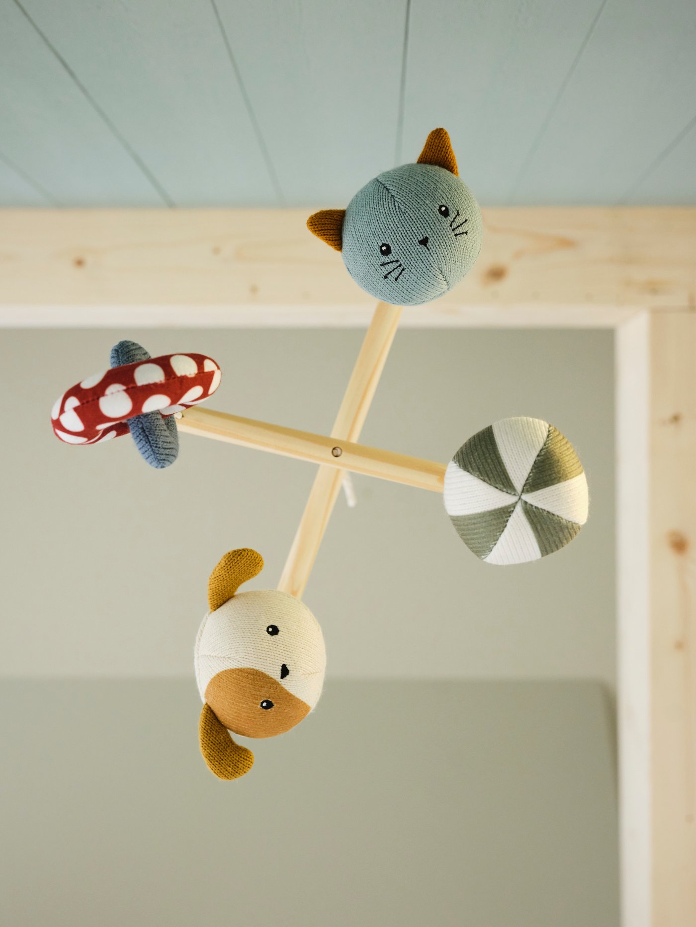 A view of a GULDVÄVARE mobile seen from below showing the faces on the soft animals attached to the mobile.