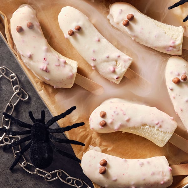 Frosty banana ghost popsicles dipped in BELÖNING white chocolate with raspberries, with a toy spider and chain on the side.