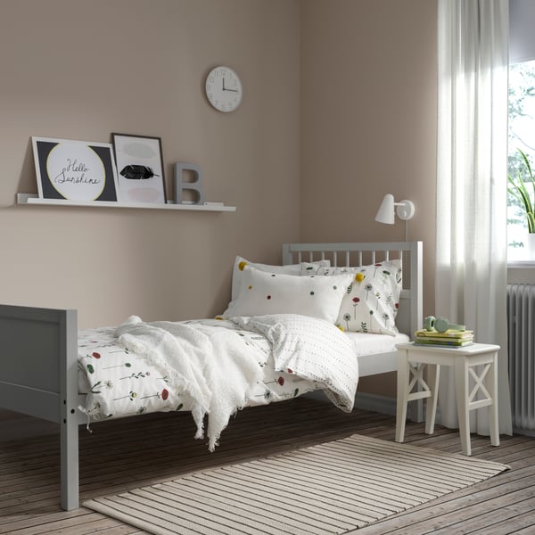 Cama juvenil de color madera color gris SMYGA vestida con ropa de cama de color blanco con pequeños estampados.