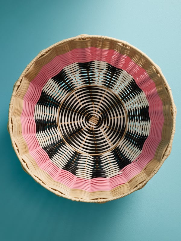 A woven DJURTRÄNARE basket with black, white, beige, and pink patterns against a teal-coloured background.