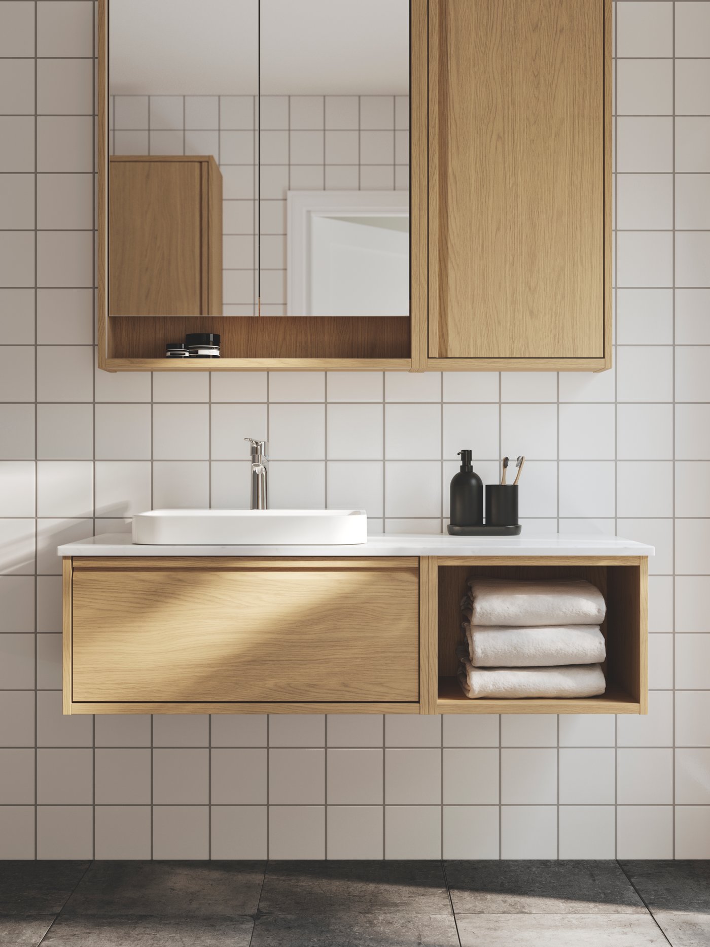 A bathroom with white tiles has an ÄNGSJÖN wash-stand in oak effect, a white semi-recessed wash-basin and a mirror cabinet.