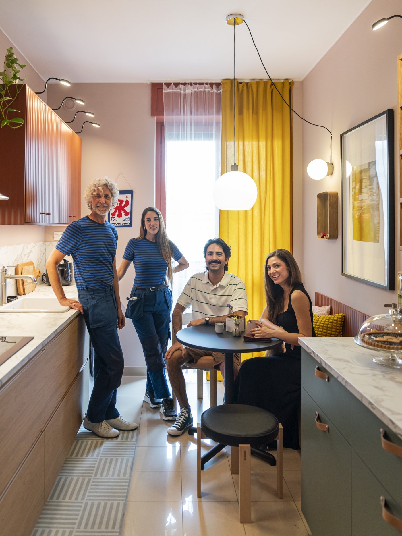Due Interior designer IKEA in divisa blu chiacchierano in cucina con due content creator seduti a un tavolo rotondo, in una cucina colorata con tende gialle e arredi moderni.