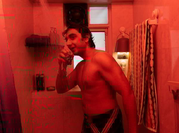 Man standing in the shower in a bathroom lit with red lighting, singing along to music coming from a VAPPEBY Bluetooth speaker.