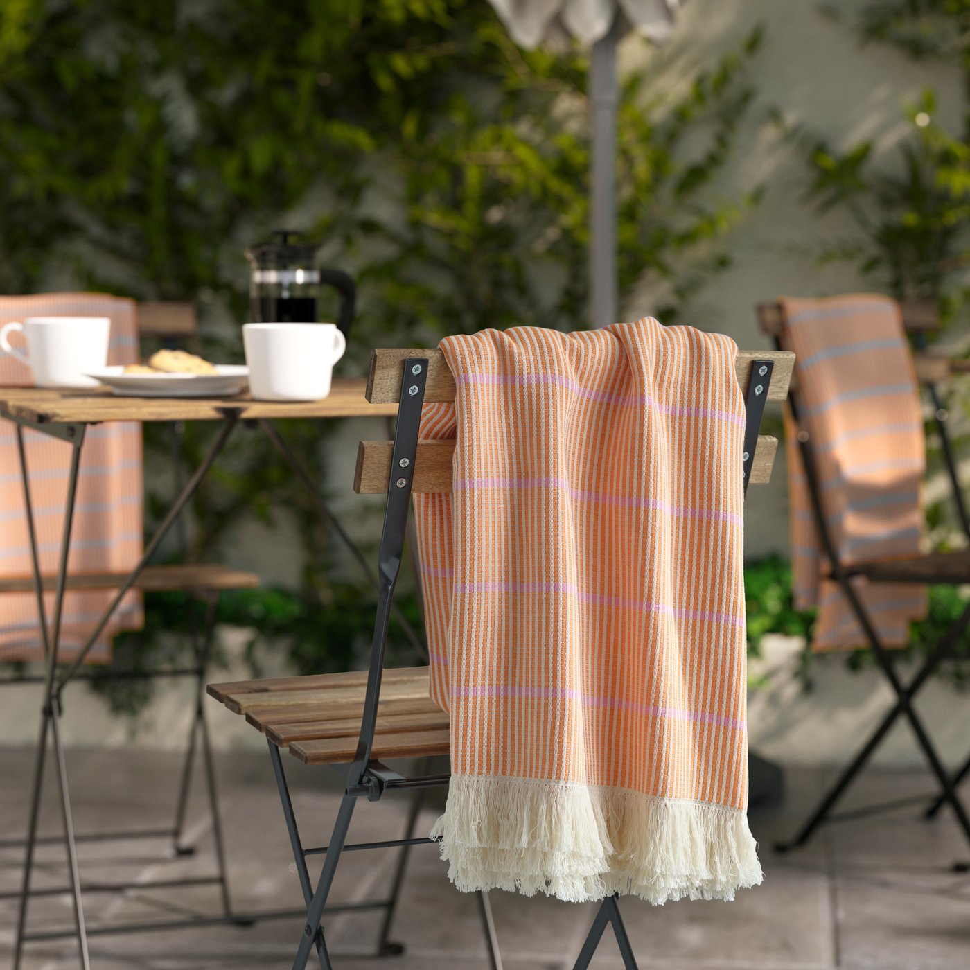 Tre plaid arancione vivo/rosa LAPPKATTFOT appoggiati su delle sedie in un giardino. 
