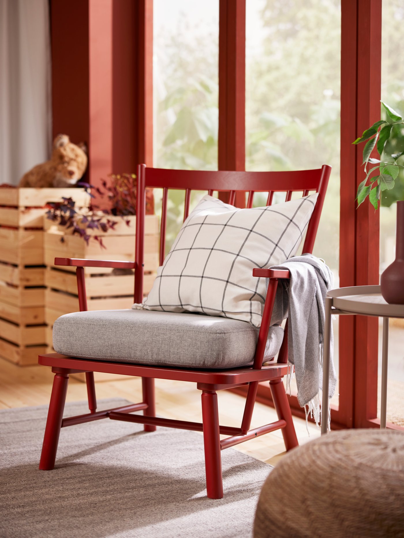 En röd PERSBOL fåtölj med en kudde i SPIKKLUBBA kuddfodral står på en grå TIDTABELL matta nära en glasdörr.