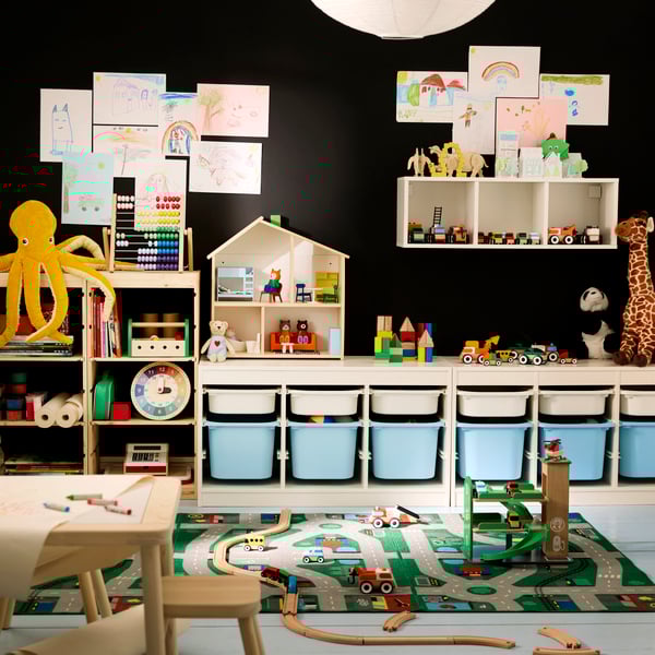 Chambre d’enfant avec mur noir dans le fond, rangement modulaire TROFAST le long du mur et tapis LILLABO sur le sol.