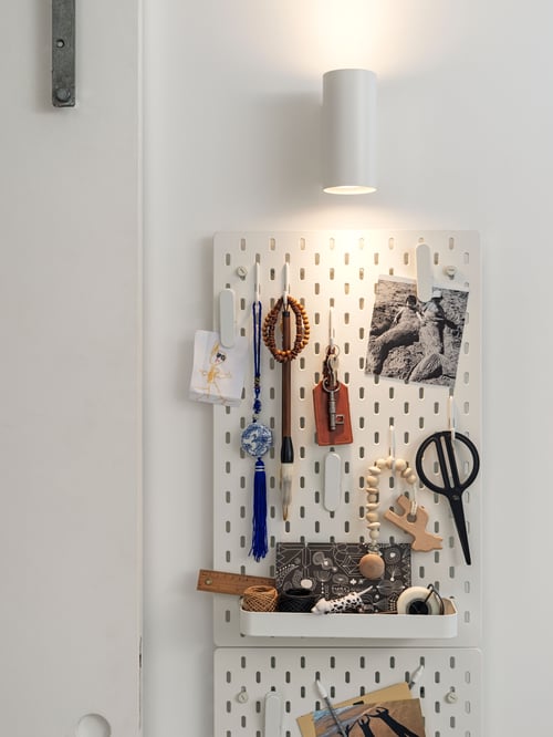 Miejsce pracy z kombinacją pegboard, biała półka ścienna, rzeczy osobiste, biały reflektor ścienny, przedmioty dekoracyjne, drzwi.