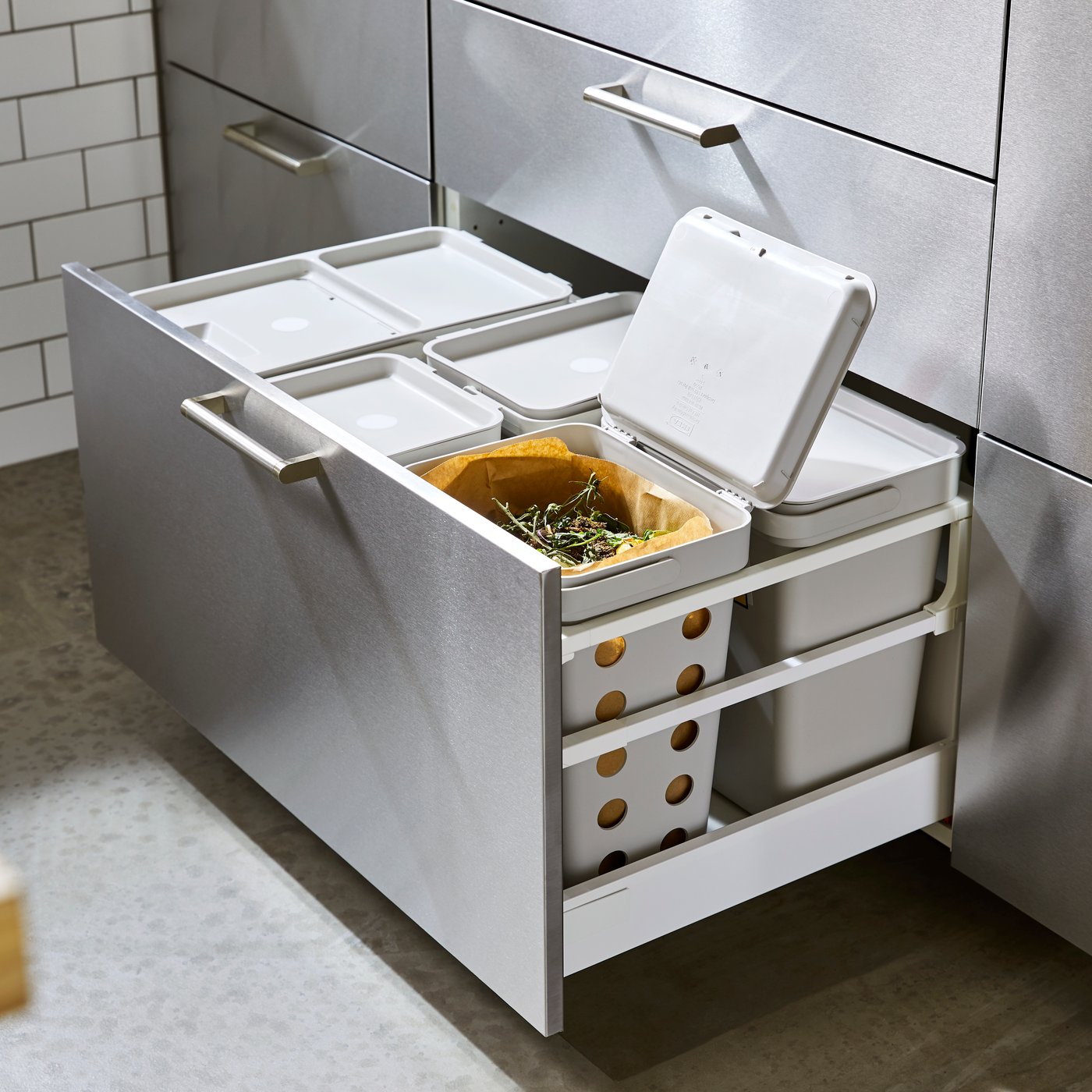 Ausgezogene Küchenschublade mit einer HÅLLBAR Abfalltrennungslösung für METOD. Ein geöffneter Deckel eröffnet den Blick auf Lebensmittelabfälle.