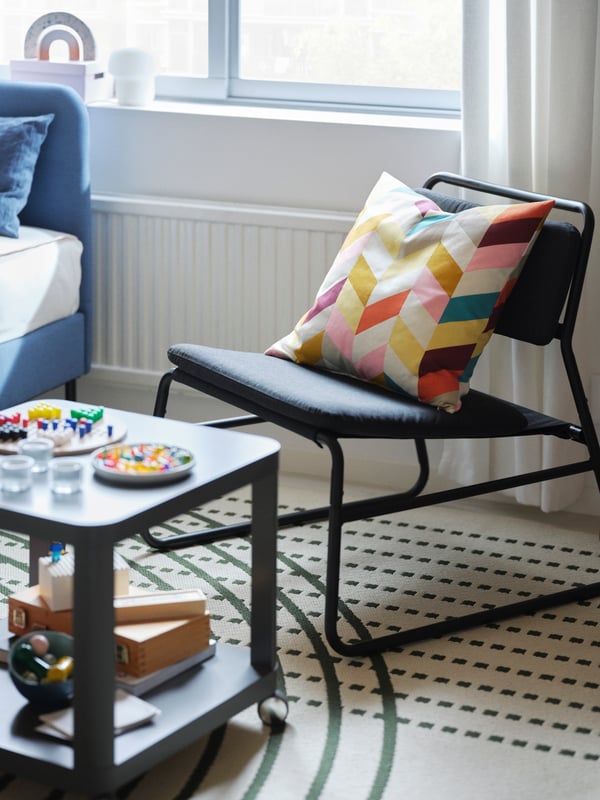 A multicolour HANNELISE cushion on a dark grey LINNEBÄCK easy chair by a grey TINGBY side table on a TÖMMERBY rug.
