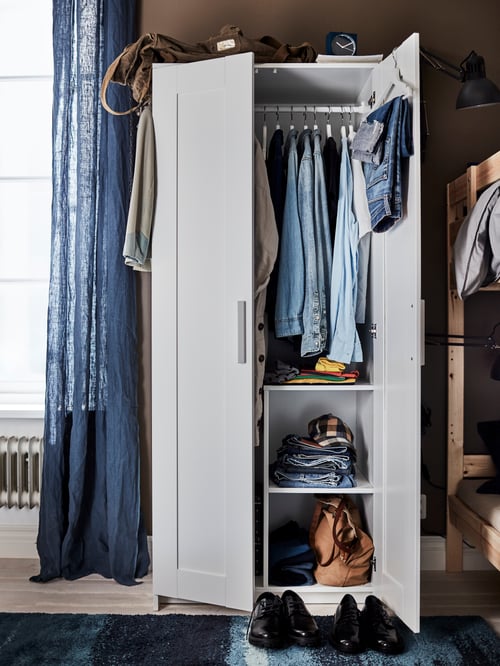 Bedroom with an open two-door wardrobe revealing multiple hanging and folded clothes, and two pairs of shoes at the base.