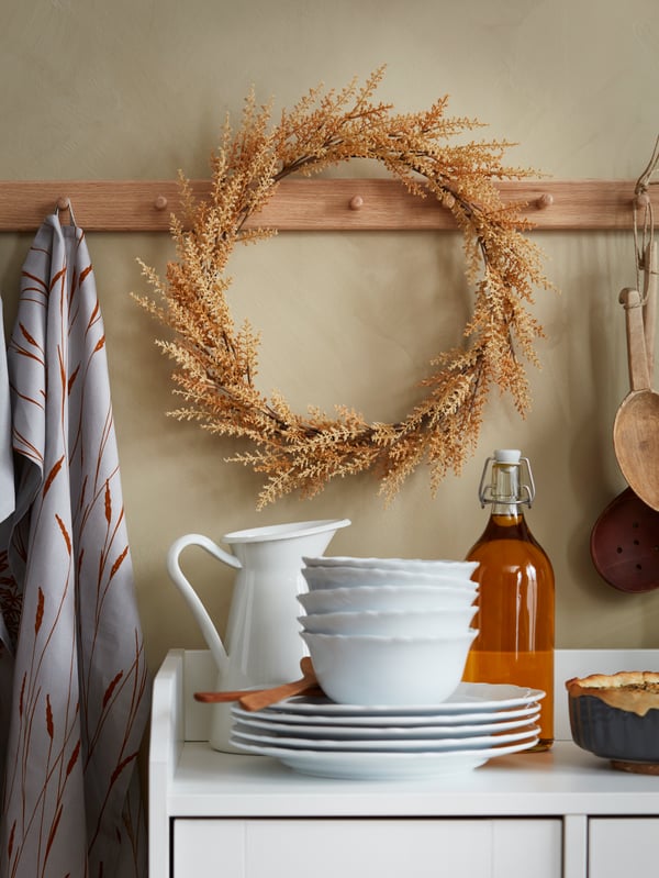 A HÖSTKVÄLL artificial wreath hangs on a knob rack with a HÖSTKVÄLL tea towel. On the sideboard is a grey HÖSTKVÄLL pie dish.