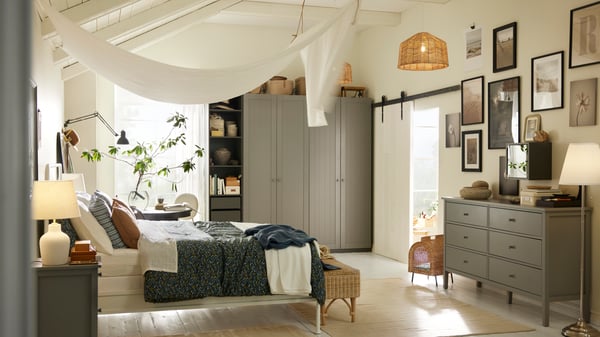 A STJÄRNÖ bed in a bright white bedroom in front of a dark grey/grey PAX/GULLABERG wardrobe combination and a black table.
