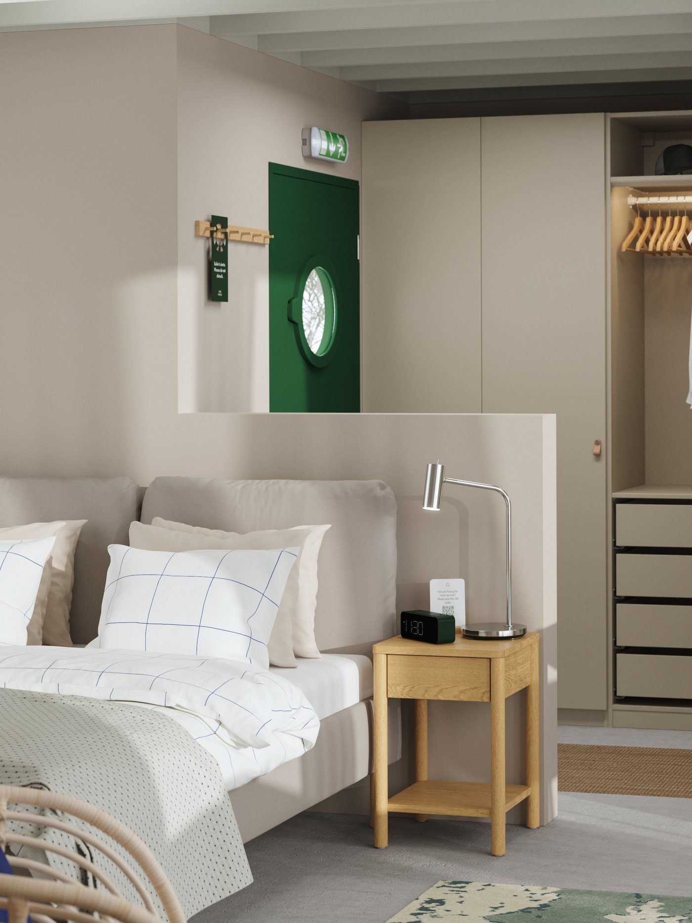 A hotel room with a green front door, a SAGESUND upholstered bed, a bedside table, a PAX wardrobe and a slim desk.