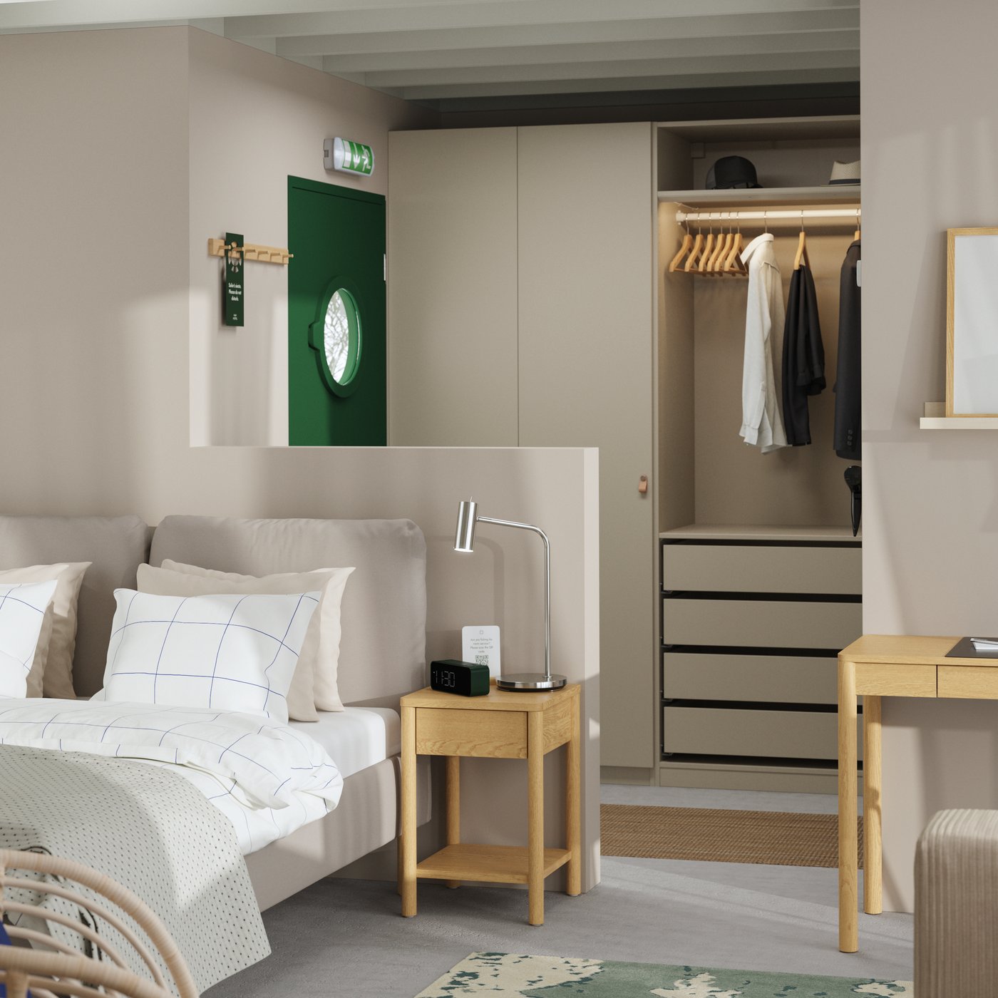 A hotel room with a green front door, a SAGESUND upholstered bed, a bedside table, a PAX wardrobe and a slim desk.
