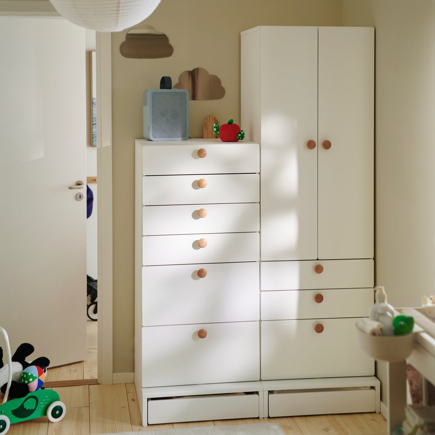 A neutral children’s room with a white SMÅSTAD/UPPFÖRA chest with 6 drawers and matching wardrobe, with round wooden knobs.