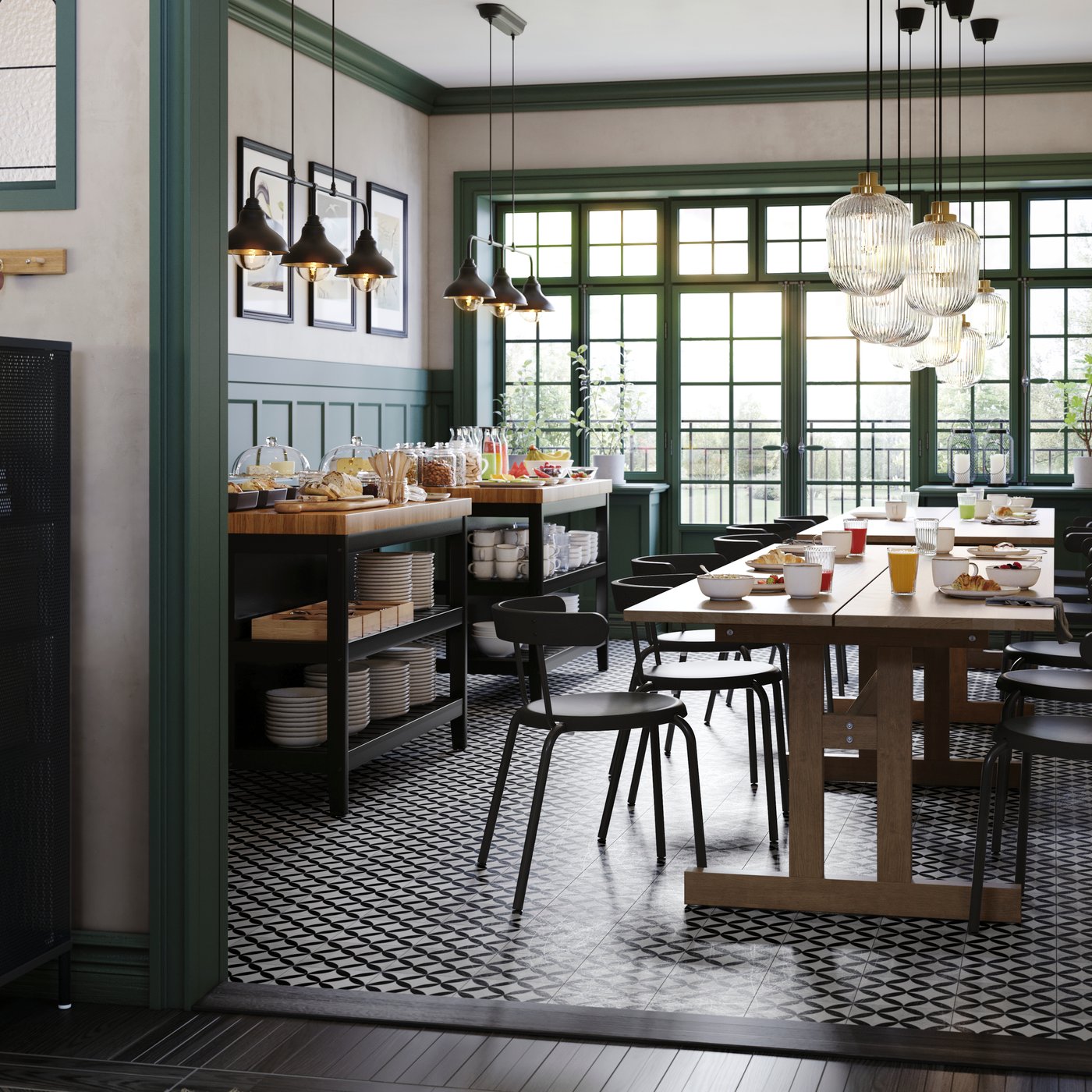 Matsal i caféstil sedd genom en öppning, med långbord dukat för frukost, svarta stolar, serveringsbord med mat och stora fönster med gröna ramar och hängande lampor.