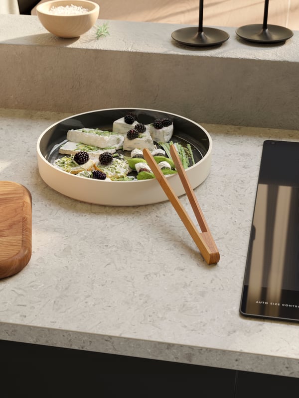 An OMBONAD serving plate in dark grey containing a cheese salad with berries, and an OSTBIT serving tong in bamboo.