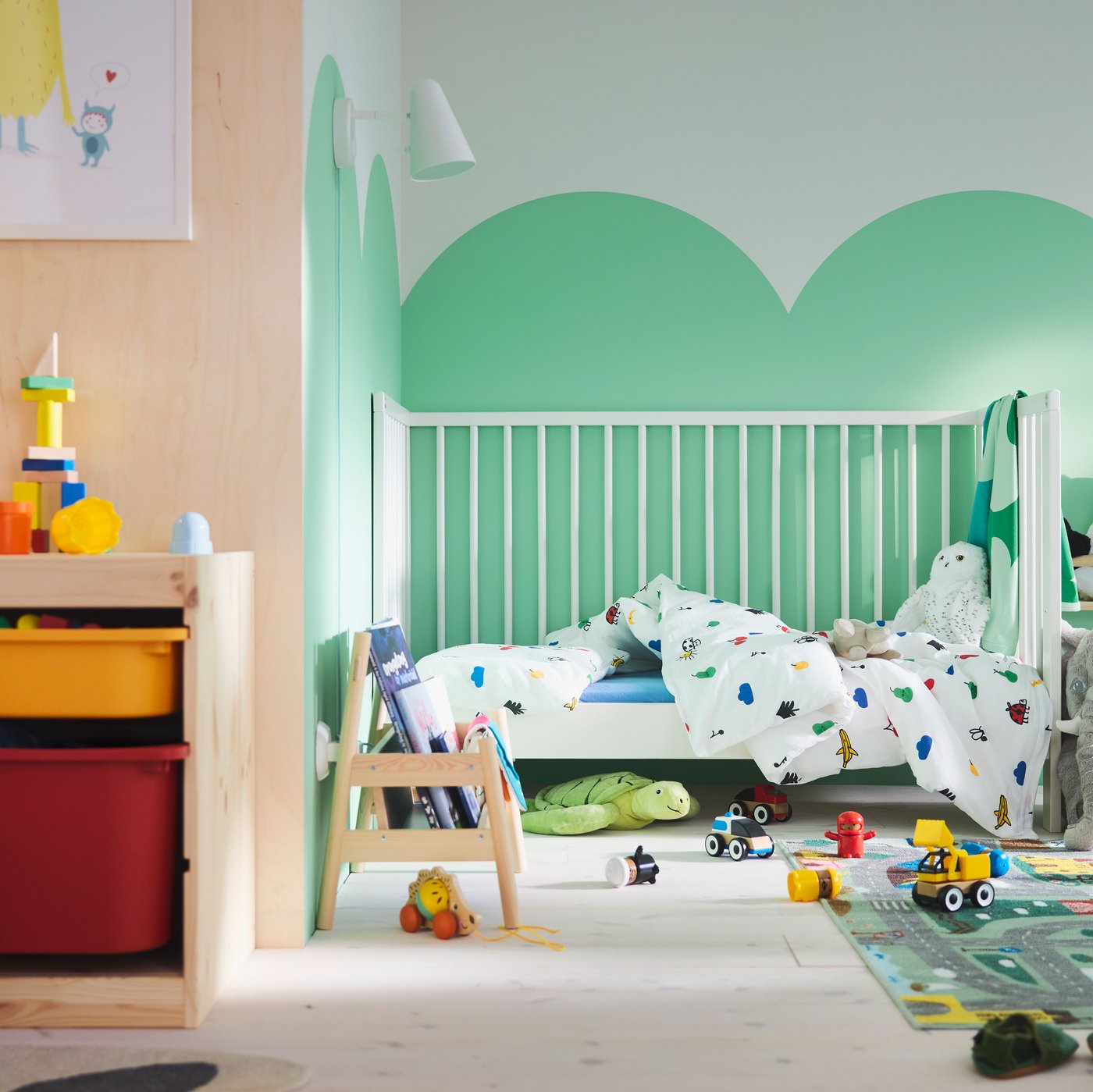 Habitación infantil con nubes verdes pintadas en la pared, cuna GULLIVER al fondo, alfombra VALLABY y muchos coches de juguete en el suelo.
