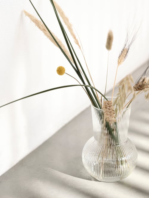 Un vase PÅDRAG est posé au sol dans un décor minimaliste et rempli de fleurs séchées et de blé pour un aspect rustique et naturel.