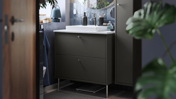 A small bathroom has a dark grey HAVBÄCK washstand with two drawers, a white ORRSJÖN washbasin and a round FAXÄLVEN mirror.
