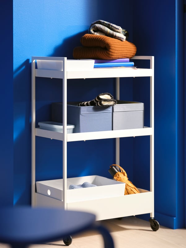 A white NISSAFORS trolley with blue and grey DRÖNA boxes on the middle shelf and a white KUGGIS box on the low shelf.