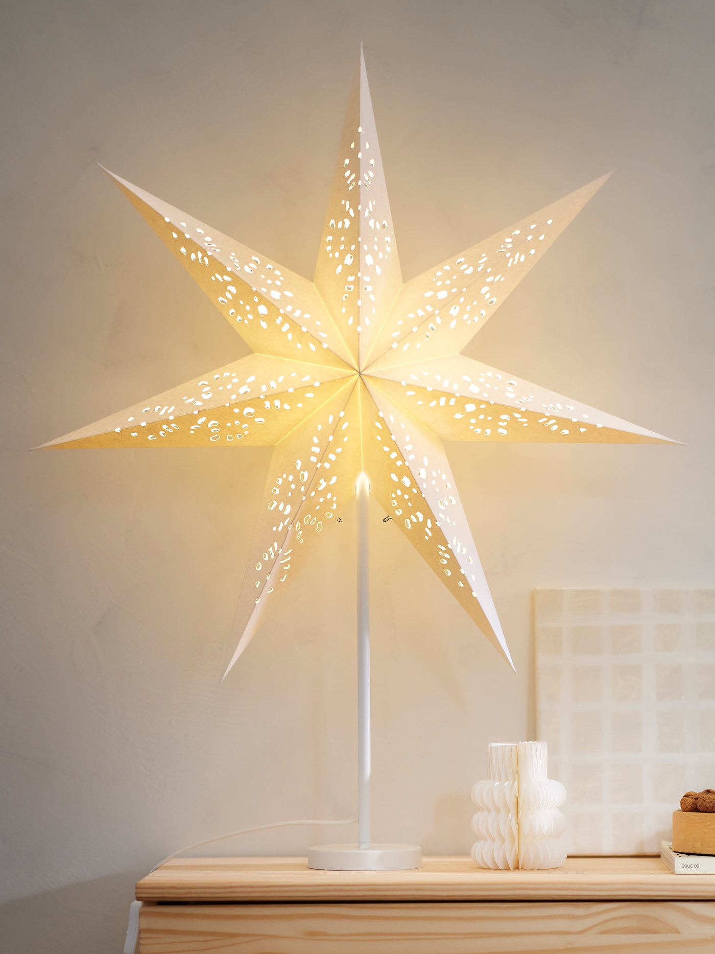 Lysande stjärnformad lampa i ett ljust och stilrent rum ovanför en träbyrå.
