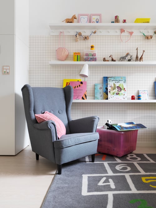 Kinderzimmer mit einem STRANDMON Kindersessel, einem HEMMAHOS Teppich, einer FUBBLA LED-Arbeitsleuchte und zwei LURT Leisten mit 6 Knöpfen.